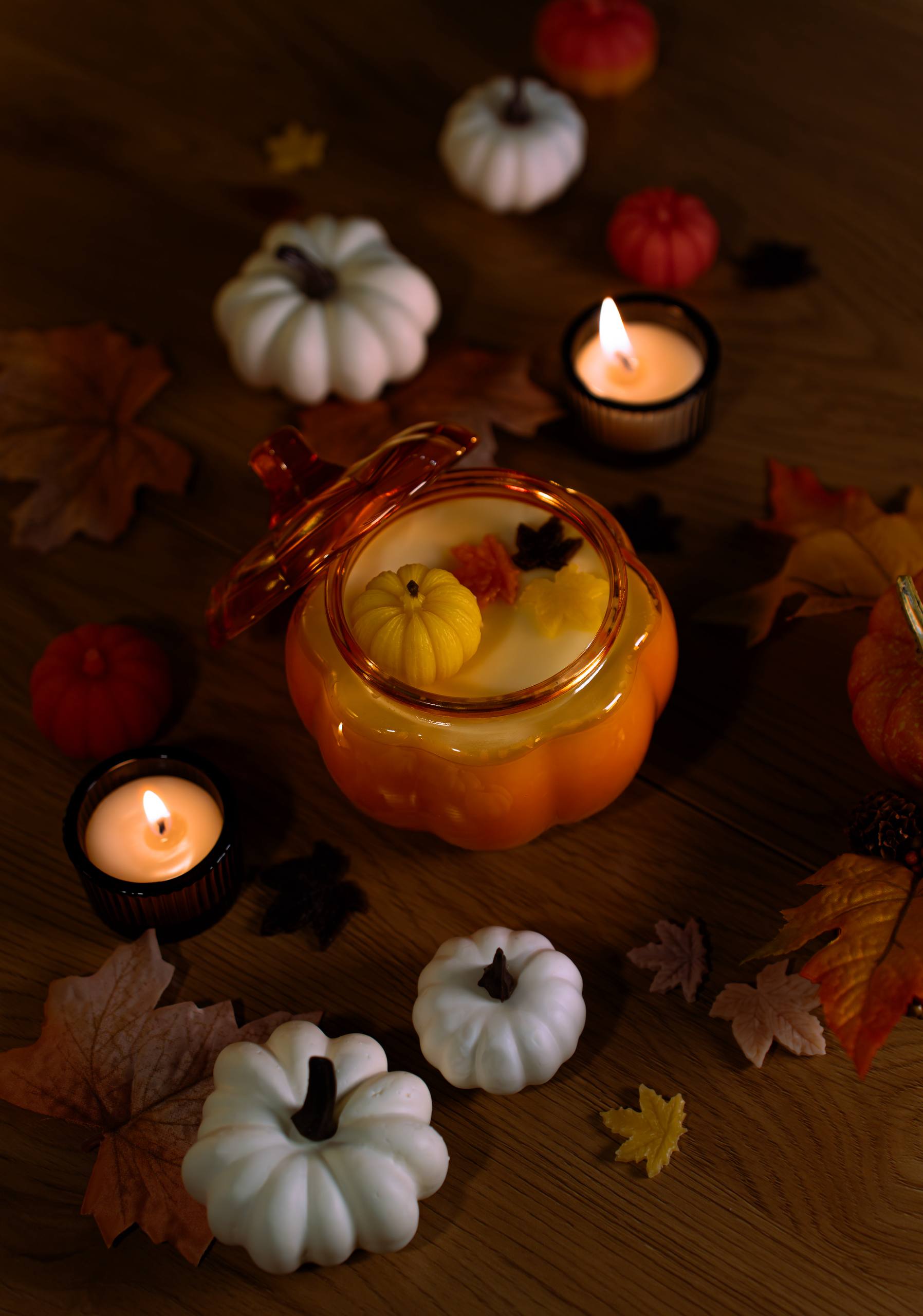 Candlelit scene with pumpkins and autumn leaves on a wooden surface